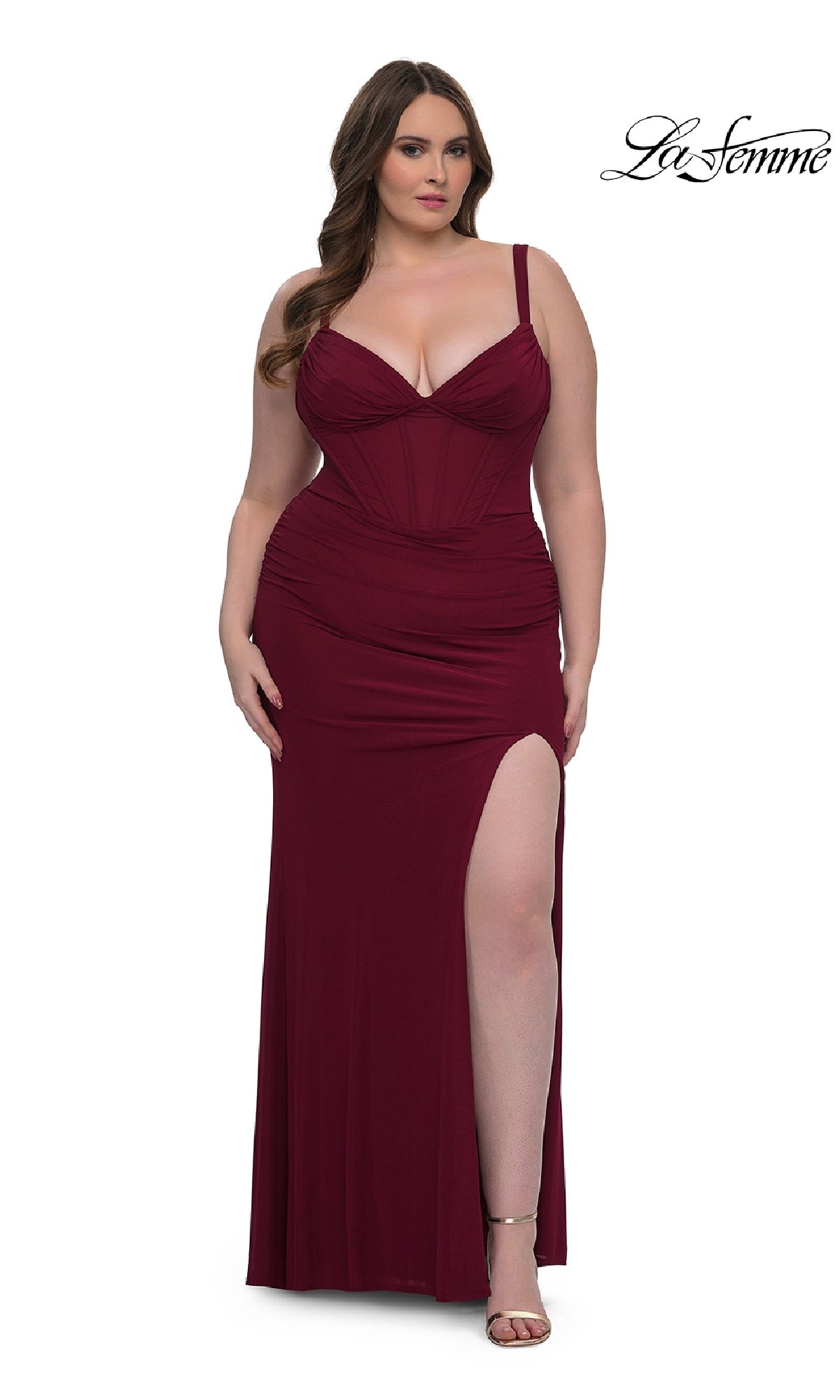 A woman poses against a white background in the Plus-Size Long Corset Prom Dress: La Femme 33015, a sleeveless burgundy gown with a thigh-high slit, as the La Femme logo appears in the corner to showcase this elegant formal dress.